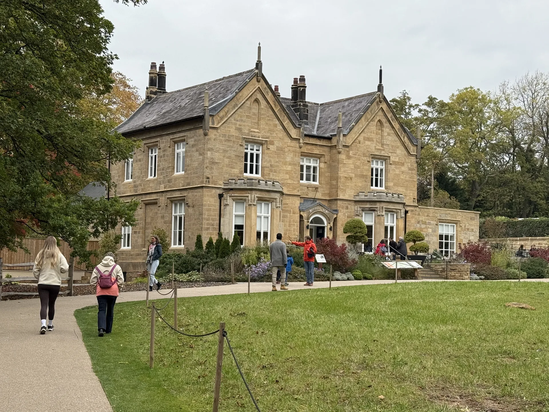 The former Harrogate Arms, a Victorian stone building at RHS Garden Harlow Carr, with visitors walking past on the garden path