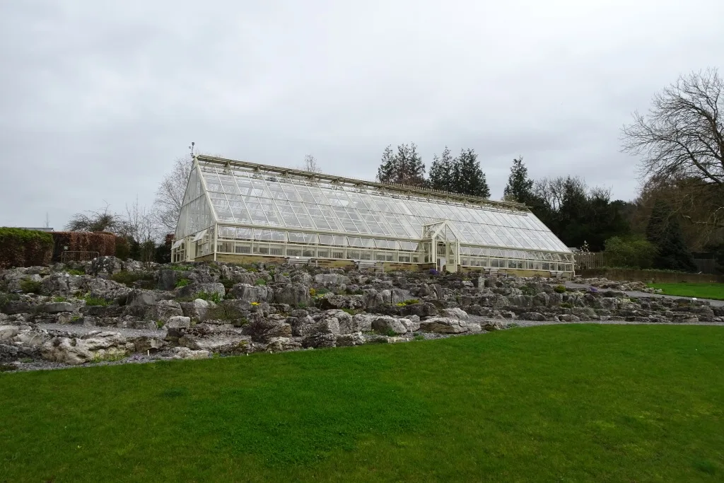 The glasshouse of the Alpine House at RHS Garden Harlow Carr above a rocky bank and lawn